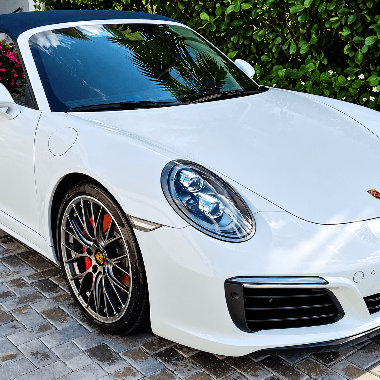 White Porsche 911 sports car with red brake calipers parked near green hedges