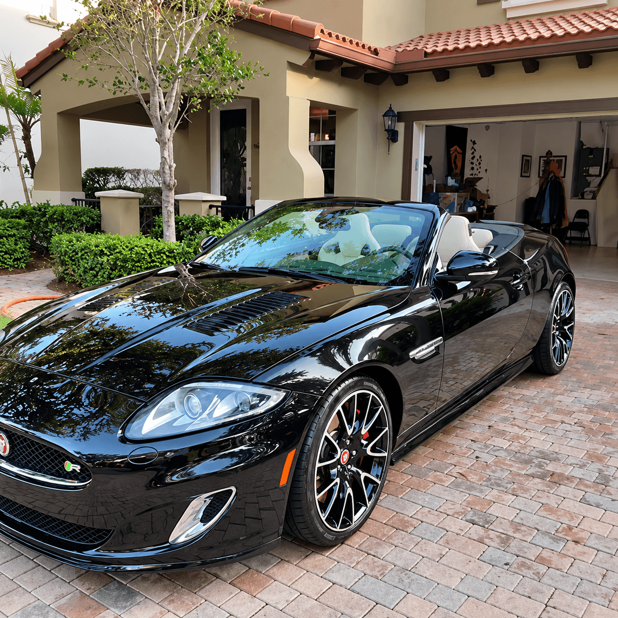 Black convertible sports car parked in front of Mediterranean-style home with terra cotta roof