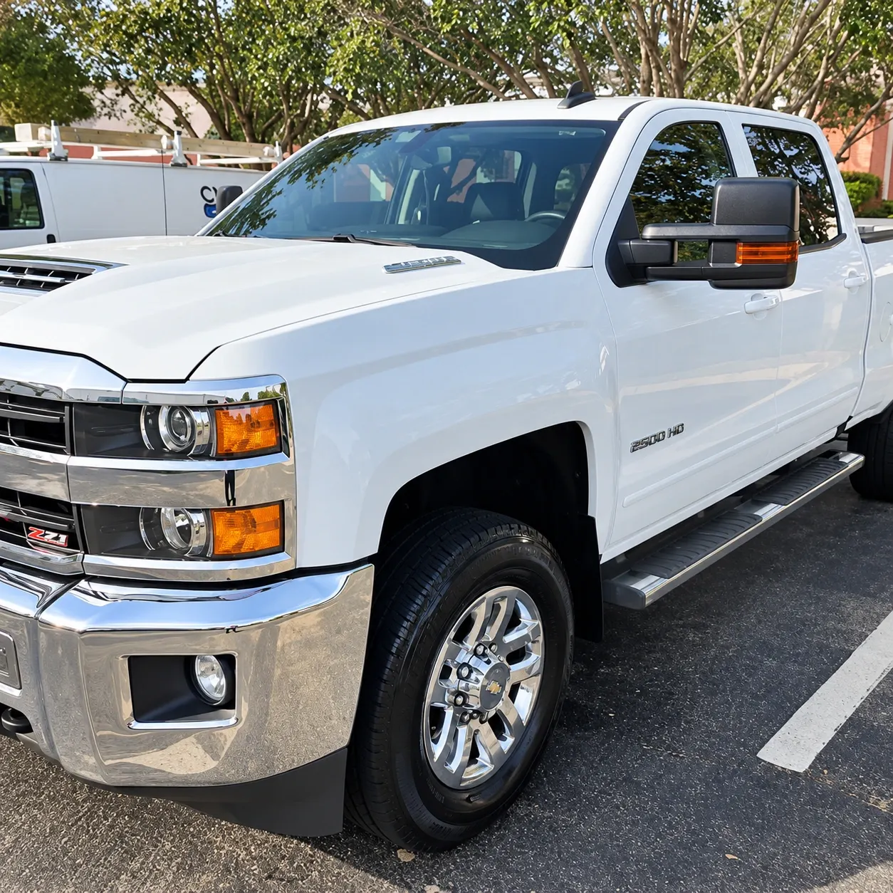 White Chevrolet Silverado 2500HD pickup truck parked in a lot with trees in background