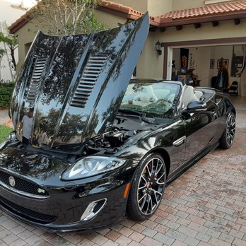 Black Jaguar XK convertible with hood and trunk open in driveway