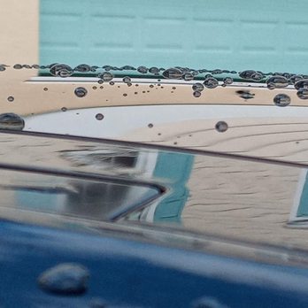 Water droplets on car windshield with blurred vehicle and garage door reflection
