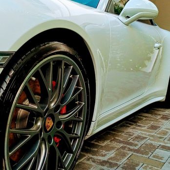 White sports car with black multi-spoke wheels and red brake calipers parked on brick pavement
