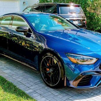 Blue sports car with black wheels parked on brick driveway beside house