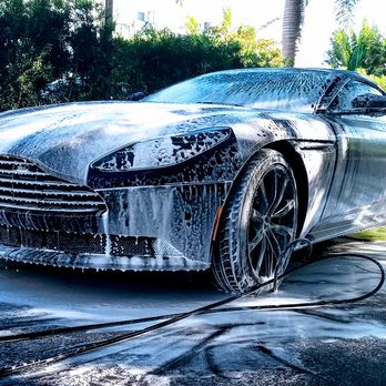 Silver luxury sports car covered in soap suds during professional car wash