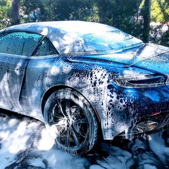 Blue sports car covered in white soap foam during outdoor wash service